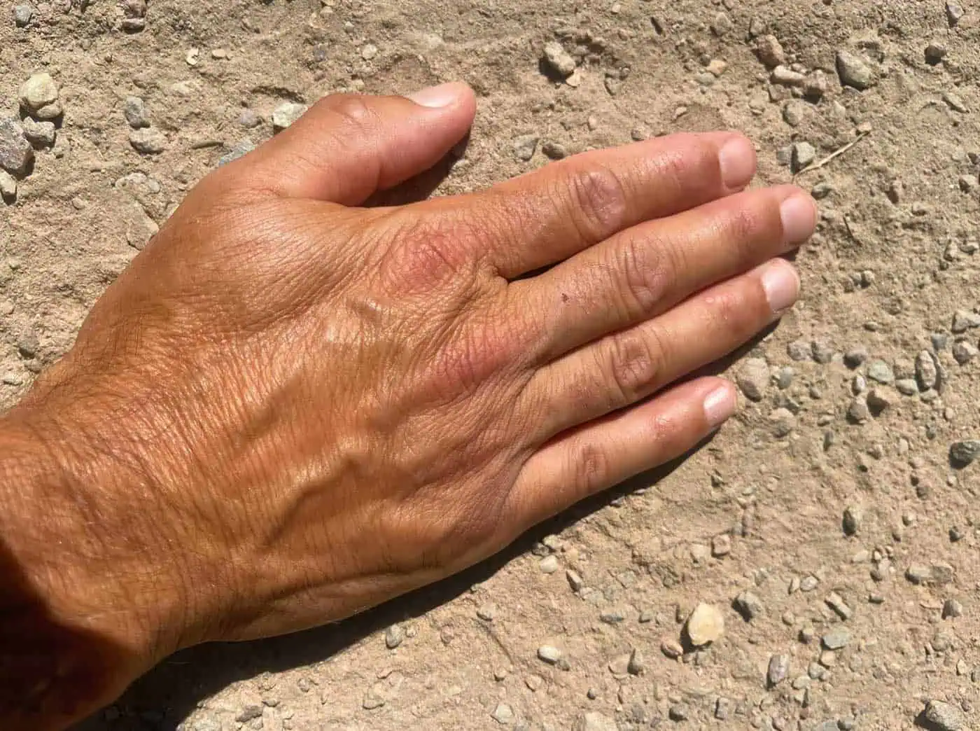 Hand op een warm, onverhard pad in de zon als contrast met heet asfalt