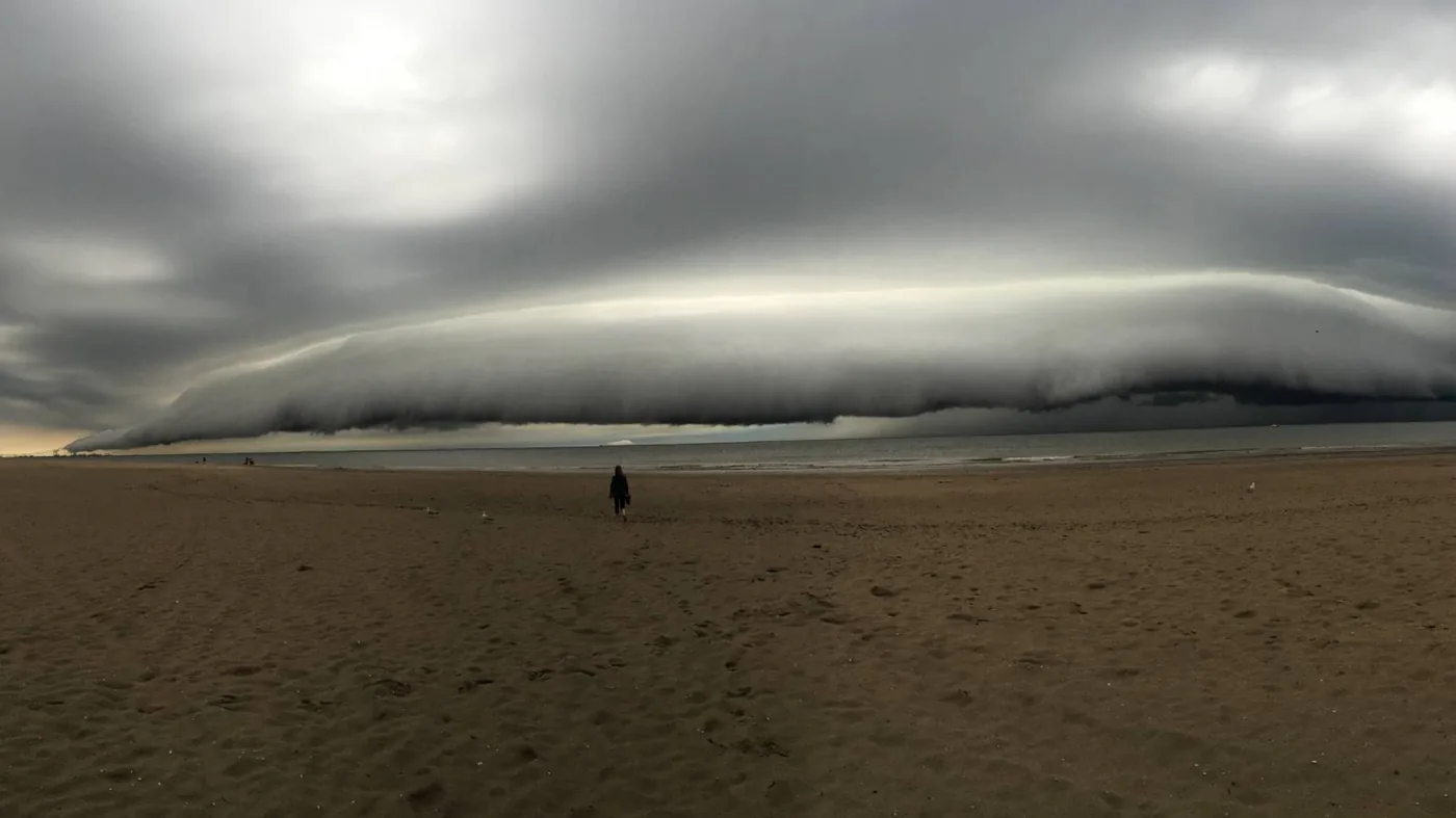 Eenzame wandelaar op een verlaten strand onder een dreigende, laaghangende onweerswolk die vanaf zee komt aanrollen