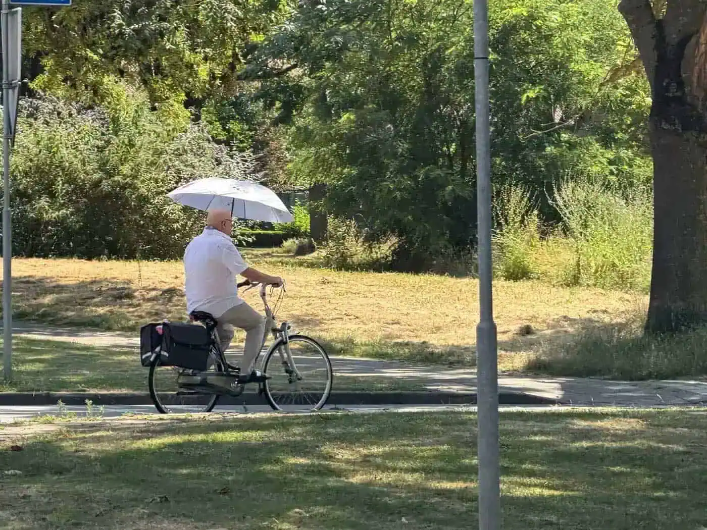Man fietst met paraplu tegen de zon tijdens hittegolf in Nederland