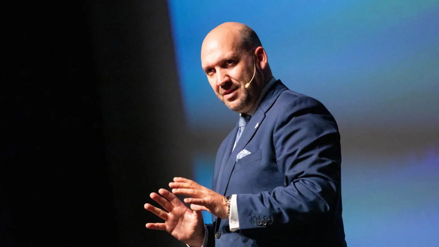 Een professionele spreker op een podium die met handgebaren uitleg geeft over het verbeteren van gastvrijheid en klantbeleving in de hospitality sector